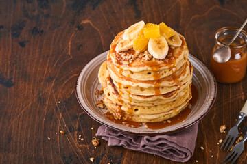 Pancakes. Homemade fluffy pancake with banana, walnut and caramel for breakfast on dark wooden background. Delicious pancakes for traditional American breakfast. Selective focus. Mock up.