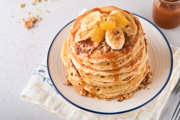 Pancakes. Homemade fluffy pancake with banana, walnut and caramel for breakfast on light concrete background. Delicious pancakes for traditional American breakfast. Selective focus. Mock up.