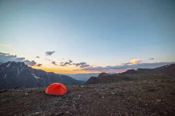 Scenic alpine landscape with tent at very high altitude with view to large mountains in orange dawn...