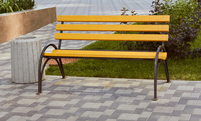 Yellow wooden metal bench and garbage can. Seating area.
