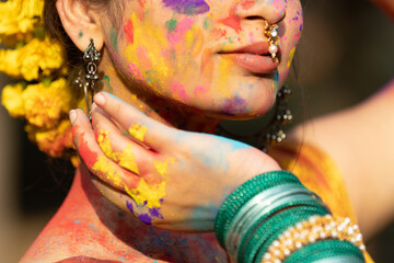 Closeup of young beautiful girl woman lady in indian attire saree with dry organic color or colour or gulal or abeer or Holi powder on her face, Holi festival of color