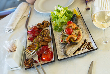 baked trout with grilled vegetables and shrimp and fresh lettuce on a white plate, food and delicacies