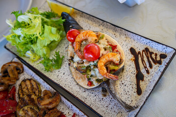 baked trout with grilled vegetables and shrimp and fresh lettuce on a white plate, food and...