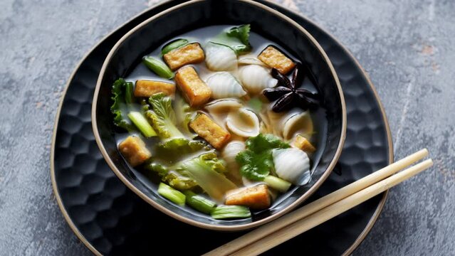 Pho soup with fried tofu cubes, noodles, pak choi and vegetables. Homemade Asian cuisine food, table spin.