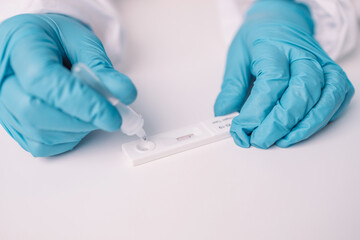 Doctor in medical PPE suit holds COVID-19 coronavirus Covid-19 rapid antigen test over blue background