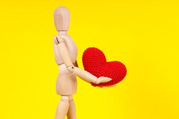 wooden man with a red heart in his hands on a yellow background
