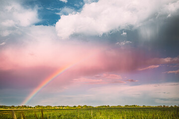 Fototapeta na wymiar Sky During Rain With Rainbow On Horizon Above Rural Landscape Field. Agricultural And Weather Forecast Concept. Countryside Meadow In Summer Rainy Day