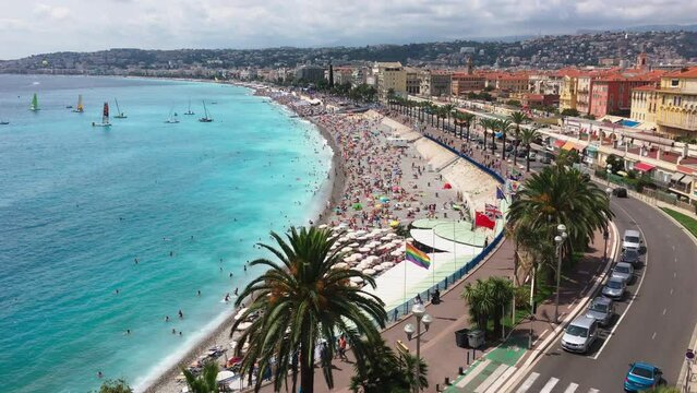 A lot of people on the main beach of Nice - France on a clear sunny day, turquoise water, umbrellas from the sun, a local attraction - the Promenade des Anglais, boats with a sail on the horizon