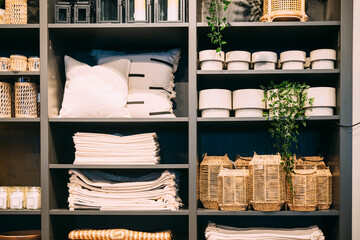 View of assortment of decor for interior shop in store of shopping center. View of shelving with pillows, plaid, baskets. View of home accessories for living room, bedroom in shop fashion retail store