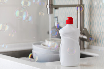 White bottle with dishwashing gel with soap bubbles around on the background of a sink with dirty...