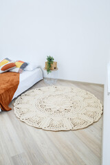 Cute homemade knitted pattern of thick threads made by hand: a handmade rug made of beige threads lies in the bedroom near the bed, the art of knitting