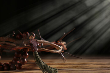 Prayer beads and crown of thorns on table against dark background
