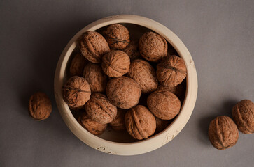 several walnuts lying in a clay bowl and next to it on a gray matte background