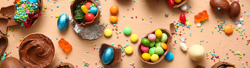 Tasty chocolate Easter eggs with different candies on beige background