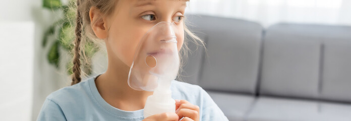 Nine years old kid with allergic asthma, inhaling her medication through spacer while looking at...
