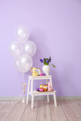 Easter cakes, eggs, vase with flowers and stylish decor on stepladder stool near color wall in room