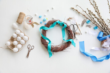 Easter wreath with ribbon, eggs, scissors and pussy willow branches on white table
