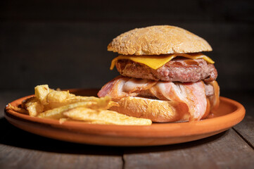 Premium grilled beef hamburger with bacon, cheese and French fries. Delicious American burger on wooden background. High quality photography