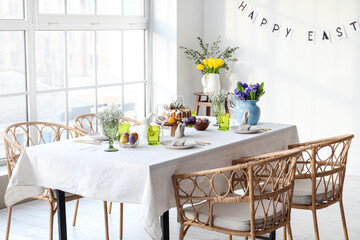 Festive dinnerware and beautiful flowers on table served for Easter celebration in light room interior