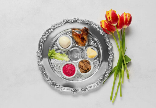 Passover Seder plate with traditional food and flowers on white background