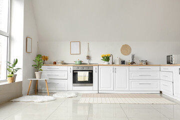 Kitchen counters with utensils and beautiful flowers near white wall in room interior