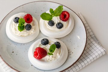 Meringue nests with whipped cream, raspberries, blueberries and a mint leaf