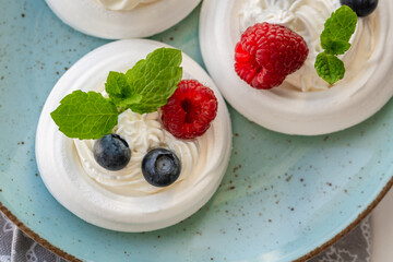 Meringue nests with whipped cream, raspberries, blueberries and a mint leaf