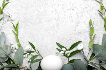 Stylish wreath with Easter eggs, eucalyptus leaves and flowers on light background