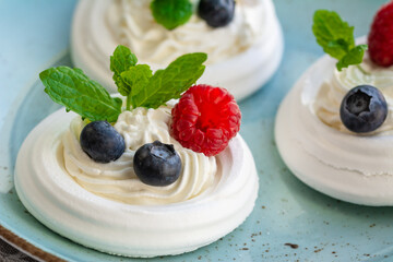 Meringue nests with whipped cream, raspberries, blueberries and a mint leaf