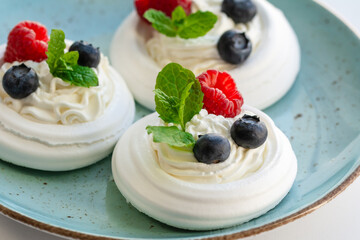 Meringue nests with whipped cream, raspberries, blueberries and a mint leaf