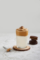 Frappé, cold coffee with milk in a glass on a wood and marble table. Spoon with dulce de leche, salted caramel and alfajores behind.