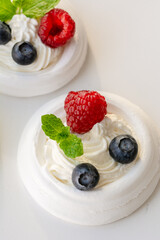 Meringue nests with whipped cream, raspberries, blueberries and a mint leaf