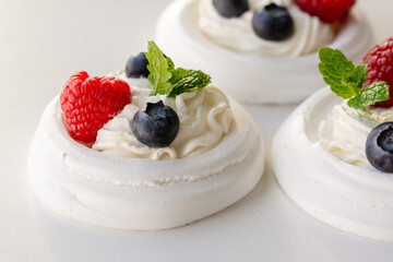 Meringue nests with whipped cream, raspberries, blueberries and a mint leaf