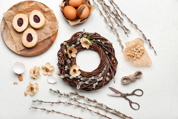 Composition with beautiful Easter wreath, pussy willow branches, eggs and cookies on light background