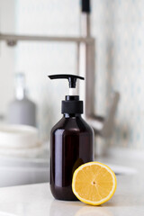 Bottle with eco friendly dishwashing detergent with lemon on the background of a sink with dirty dishes.