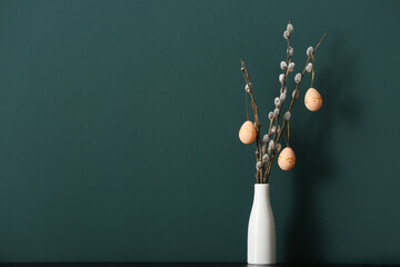 Vase with pussy willow branches and painted Easter eggs on table near green wall - obrazy, fototapety, plakaty