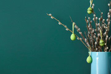 Jug with pussy willow branches and painted Easter eggs on green background, closeup © Pixel-Shot