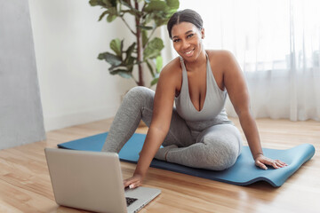African american woman working out in home livingroom gym with laptop