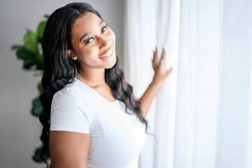 African American woman looking to aside out window, standing at home with smile