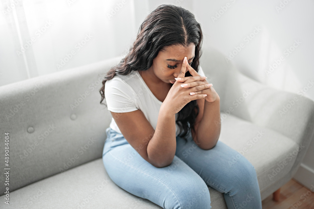 Wall mural Stressed miserable black woman suffer from grief problem, depressed lonely upset african girl crying alone on sofa