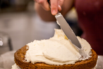 Spreading delicious, sweet frosting or icing on baked cake with knife in kitchen