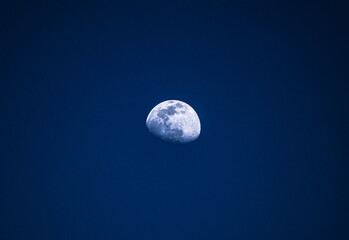 Naklejka na ściany i meble Bright partial moon in blue night sky with lit glow
