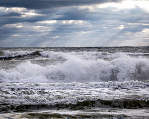 Large crashing waves and white caps on Destin Florida beach with storm clouds and sun in the background