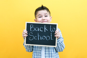 schoolboy holding a tablet in his hands with the inscription Back to school on a yellow background.