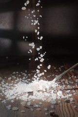 A falling of salt on a dark background, a spoonful of salt lies on top.  Coarse salt
