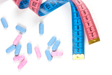 Pills with pink and blue measuring tape on white background. Concept of losing weight, diet, fat burning, healthy eating. Copy space.