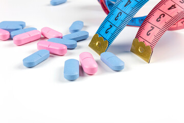Pills with pink and blue measuring tape on white background. Concept of losing weight, diet, fat burning, healthy eating. Copy space.