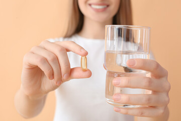 Young woman with fish oil pill and glass of water on color background, closeup