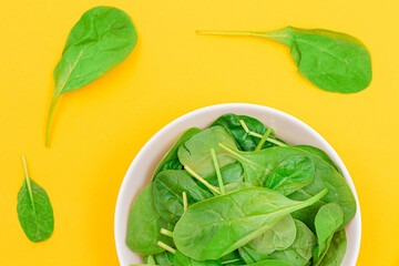 Fresh Baby Spinach Leaves in White Bowl on Yellow Background - Top View. Vegan and Vegetarian Culture. Raw Food, Green Leaves. Healthy Diet