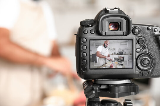 Handsome man making dough on display of photo camera in kitchen, closeup